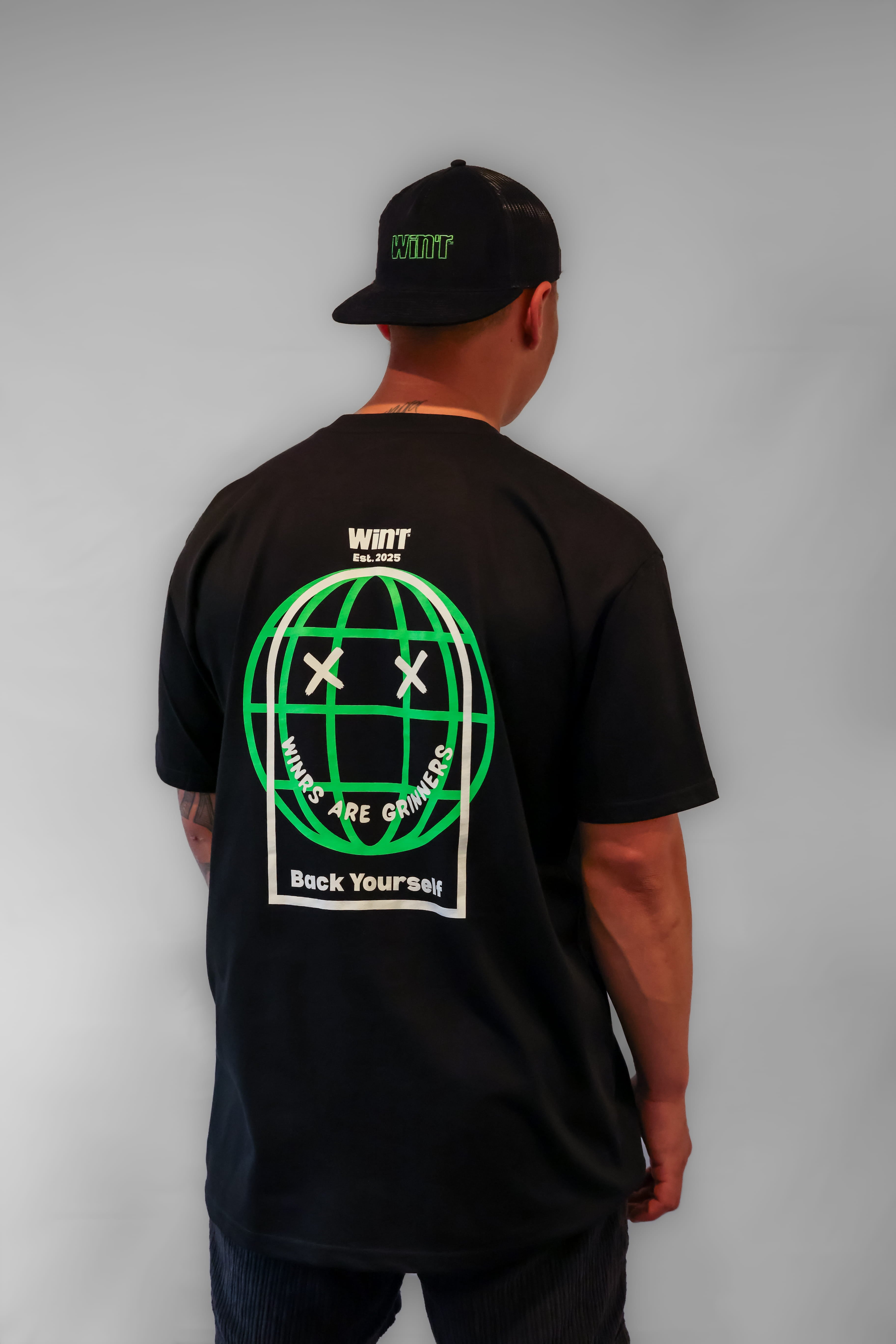 Person wearing a black Winr t-shirt with large green and white graphic on the back, premium cotton streetwear tee against a grey background.