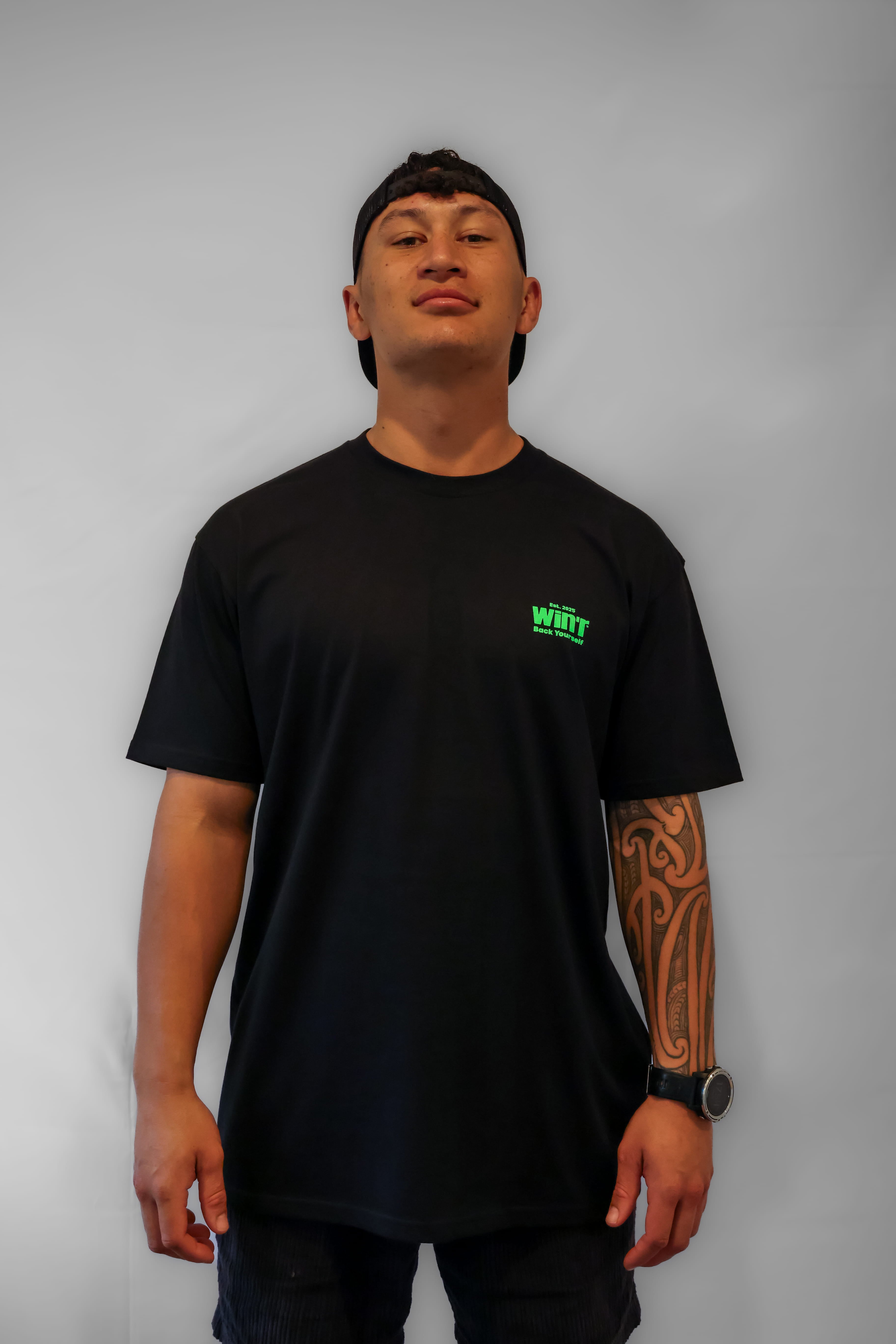 Person wearing a black t-shirt with a small green logo on a grey background