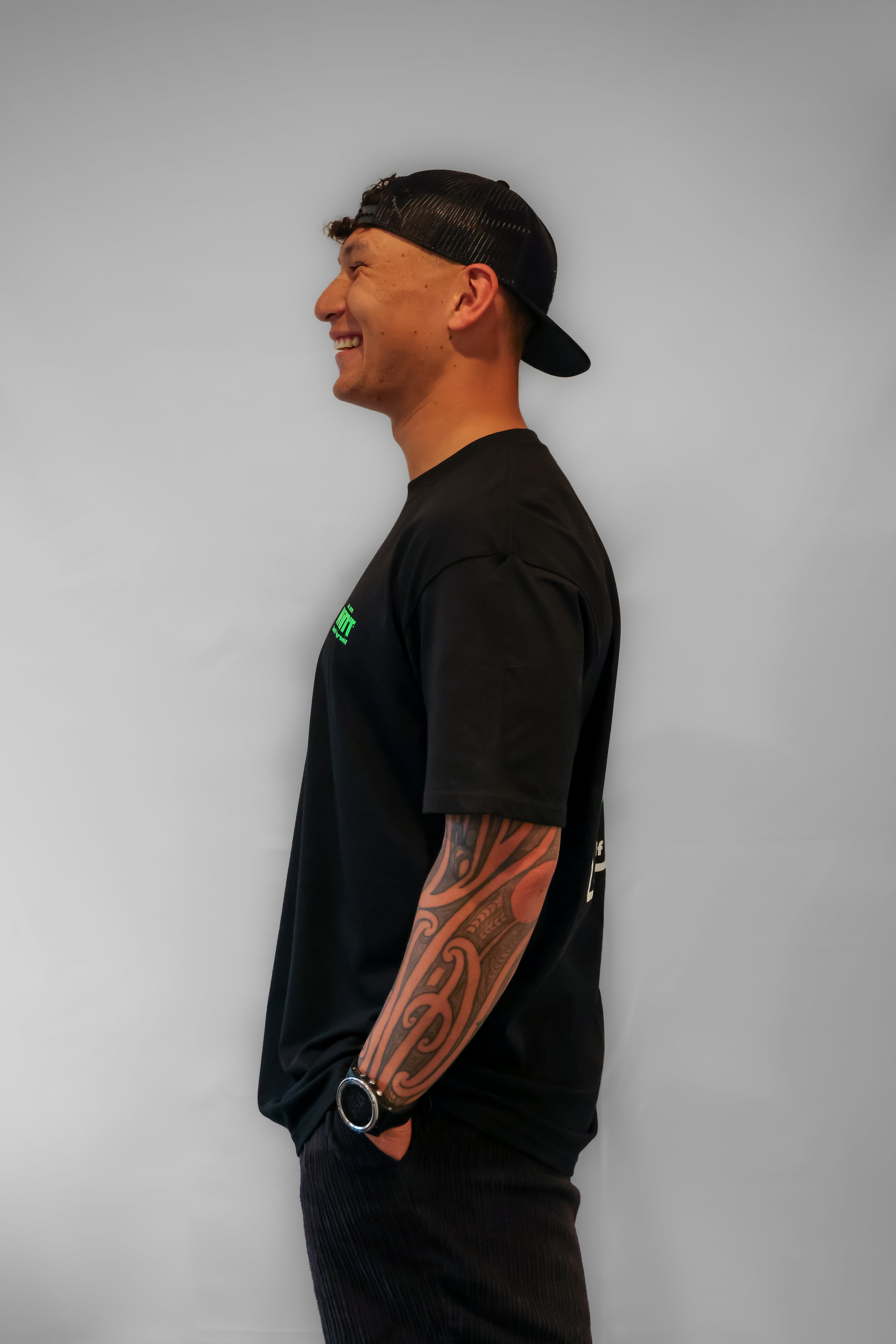 Person wearing a black t-shirt with a small green logo on a grey background
