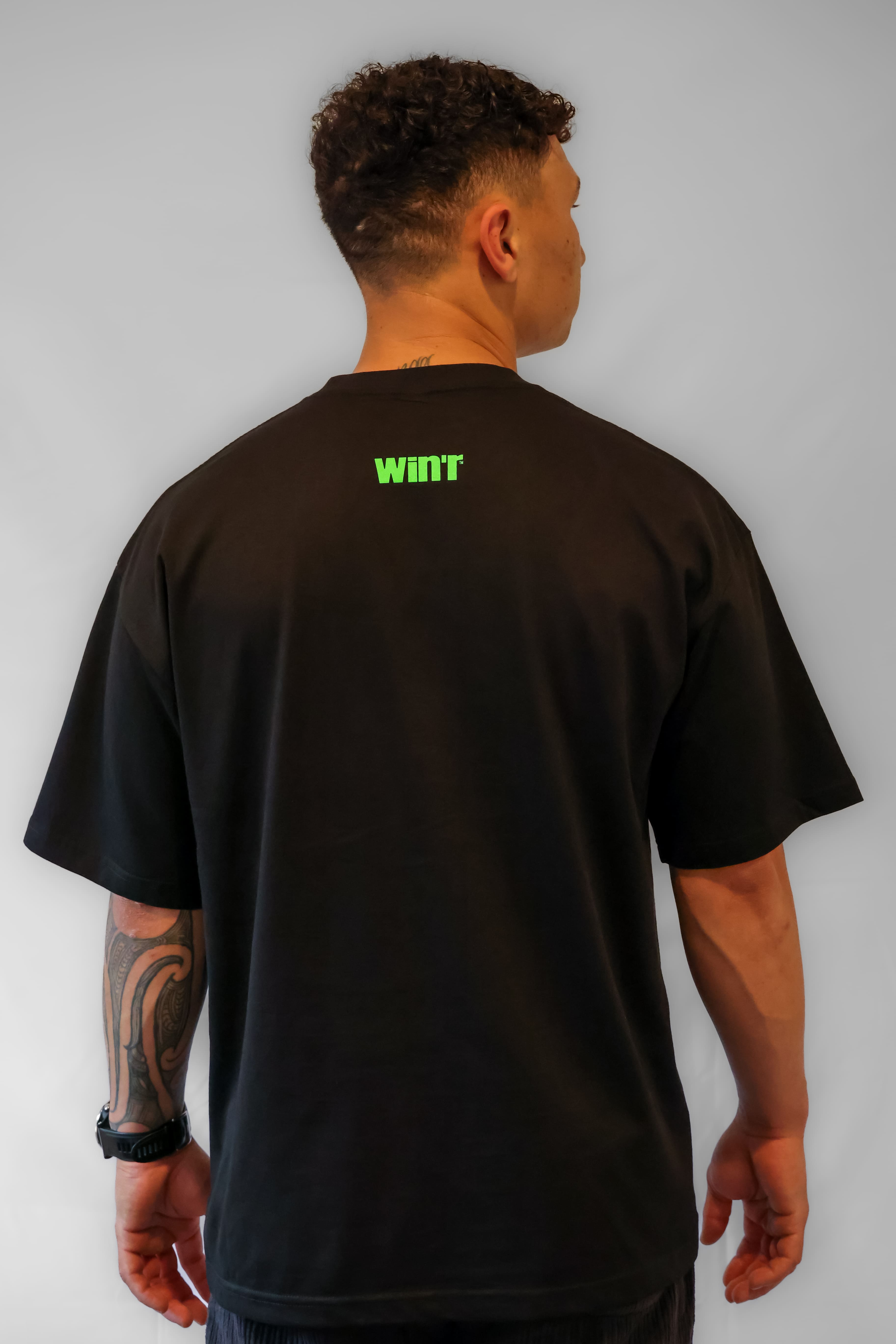 Person wearing a black oversized Winr t-shirt with small green text on the back, premium cotton streetwear tee against a grey background.