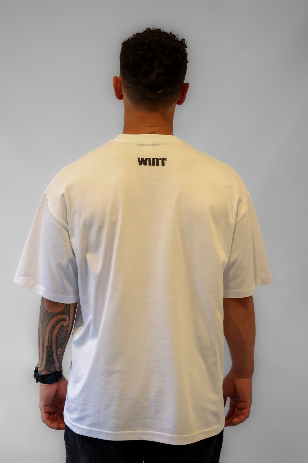 Person wearing a white Winr Statement oversized t-shirt with small black logo on the back against a grey background.