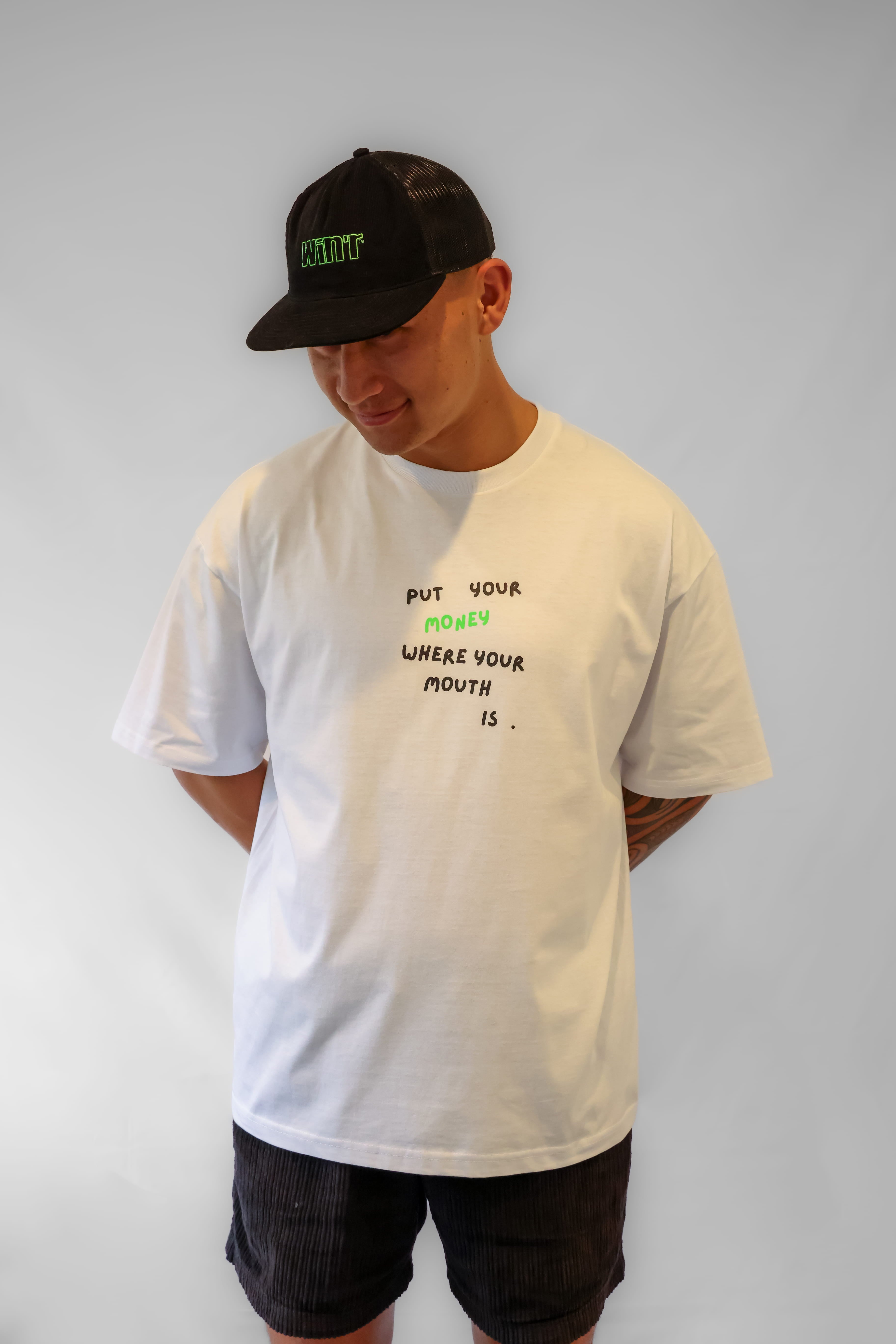 Person wearing a white oversized t-shirt with text and a black cap on a plain background