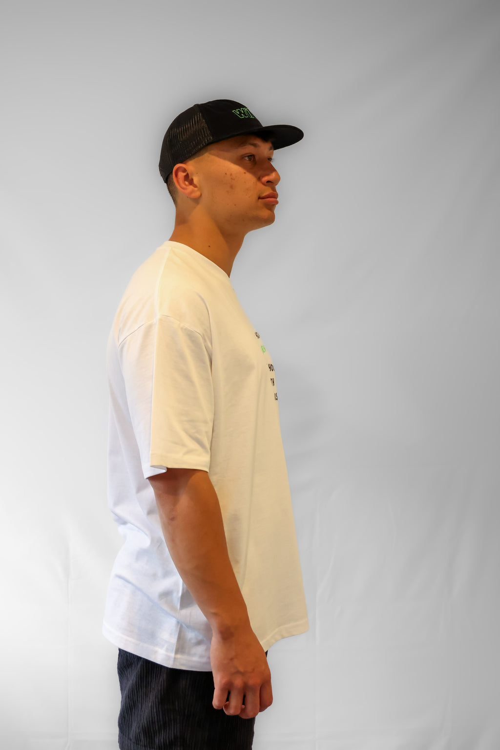 Man wearing a white oversized t-shirt with a black cap on a plain background