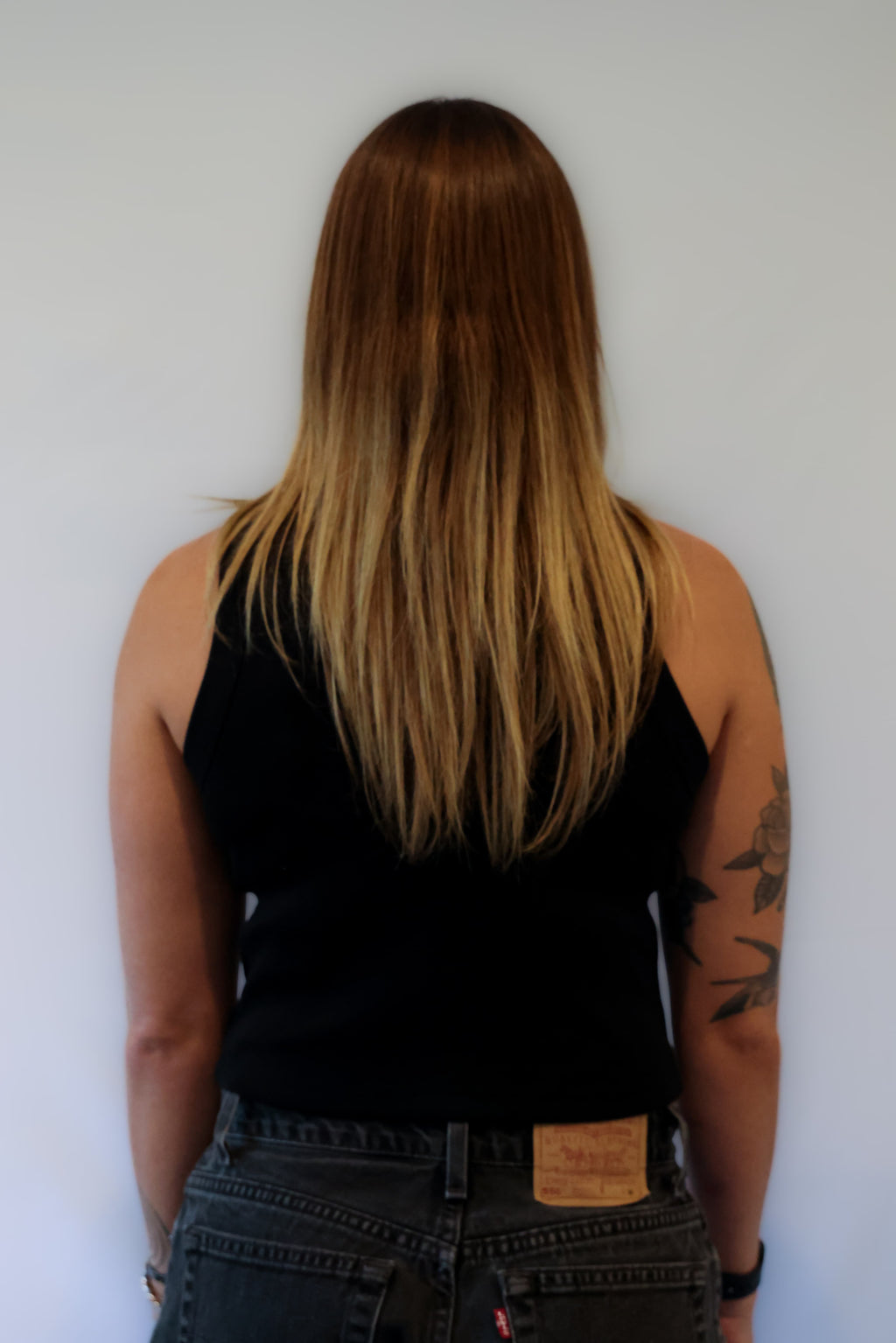 Woman wearing a black tank top and jeans against a grey background