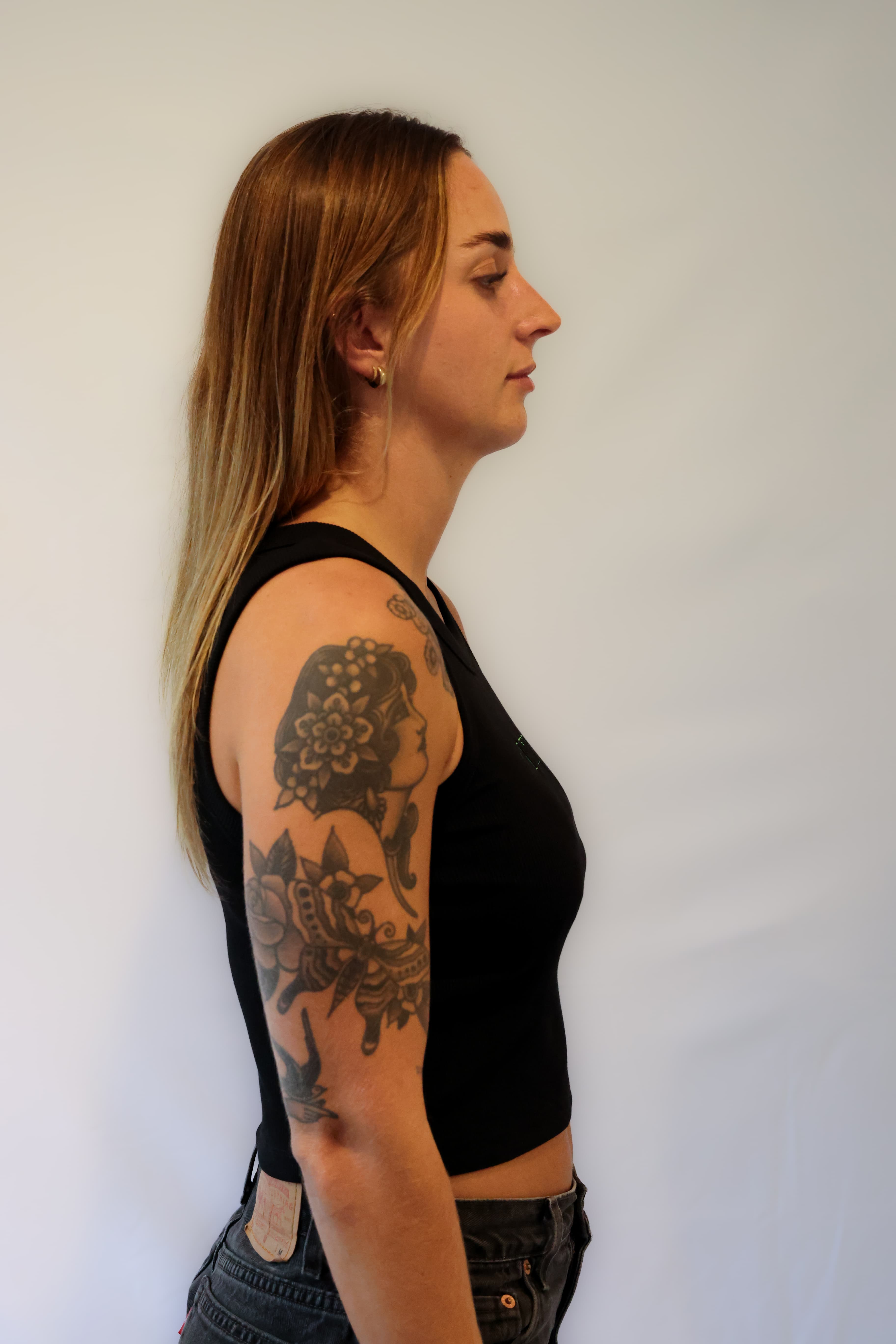 Woman with tattoos on her arms wearing a black tank top against a grey background